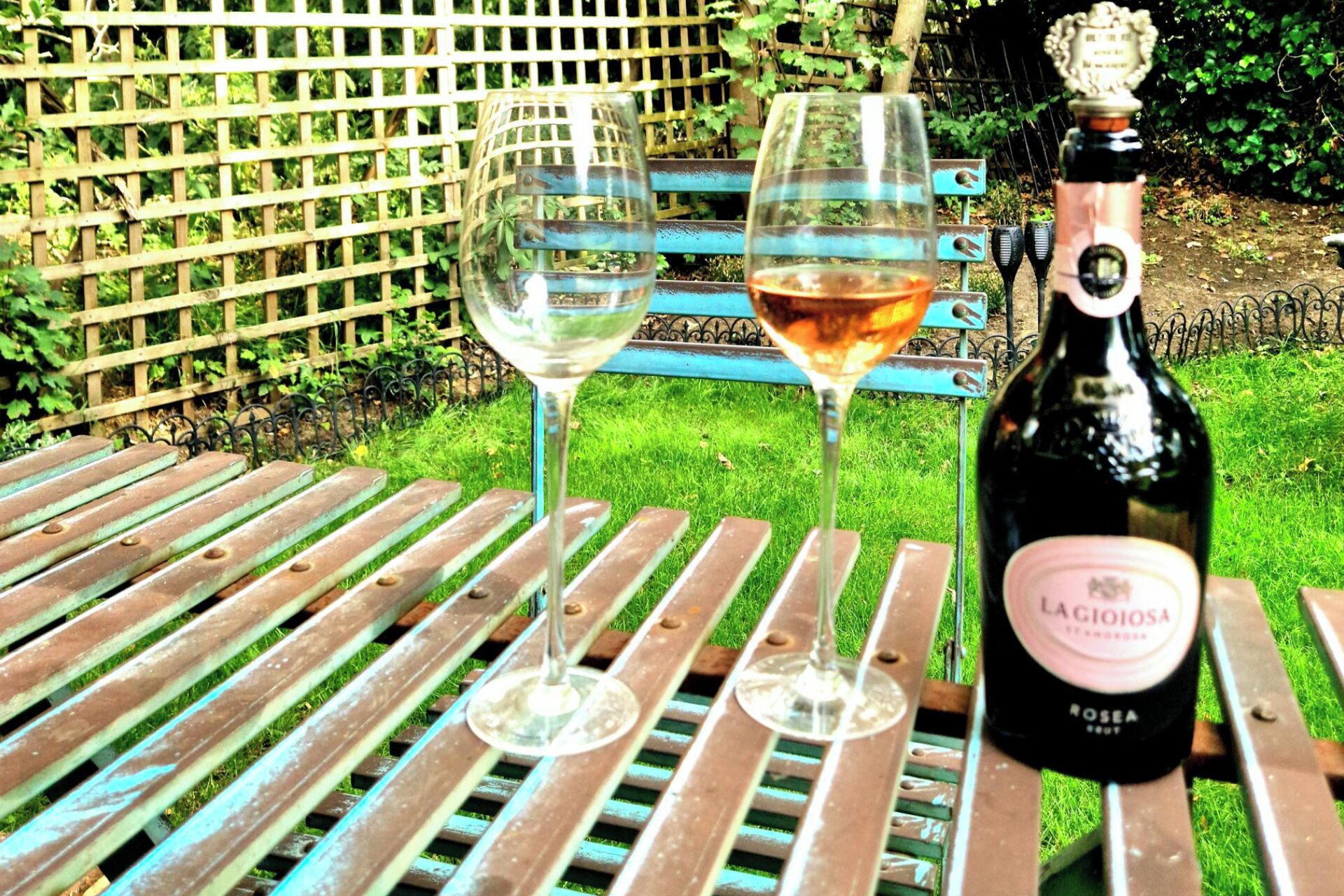 Una bottiglia di vino e due bicchieri su un tavolo in metallo all'aperto.