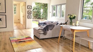 A modern living room with a sofa, a dining table with chairs, a colorful rug, and a view of greenery outside. - 1 Bed Cottage-museum View-garden-free Parking (Weybridge)