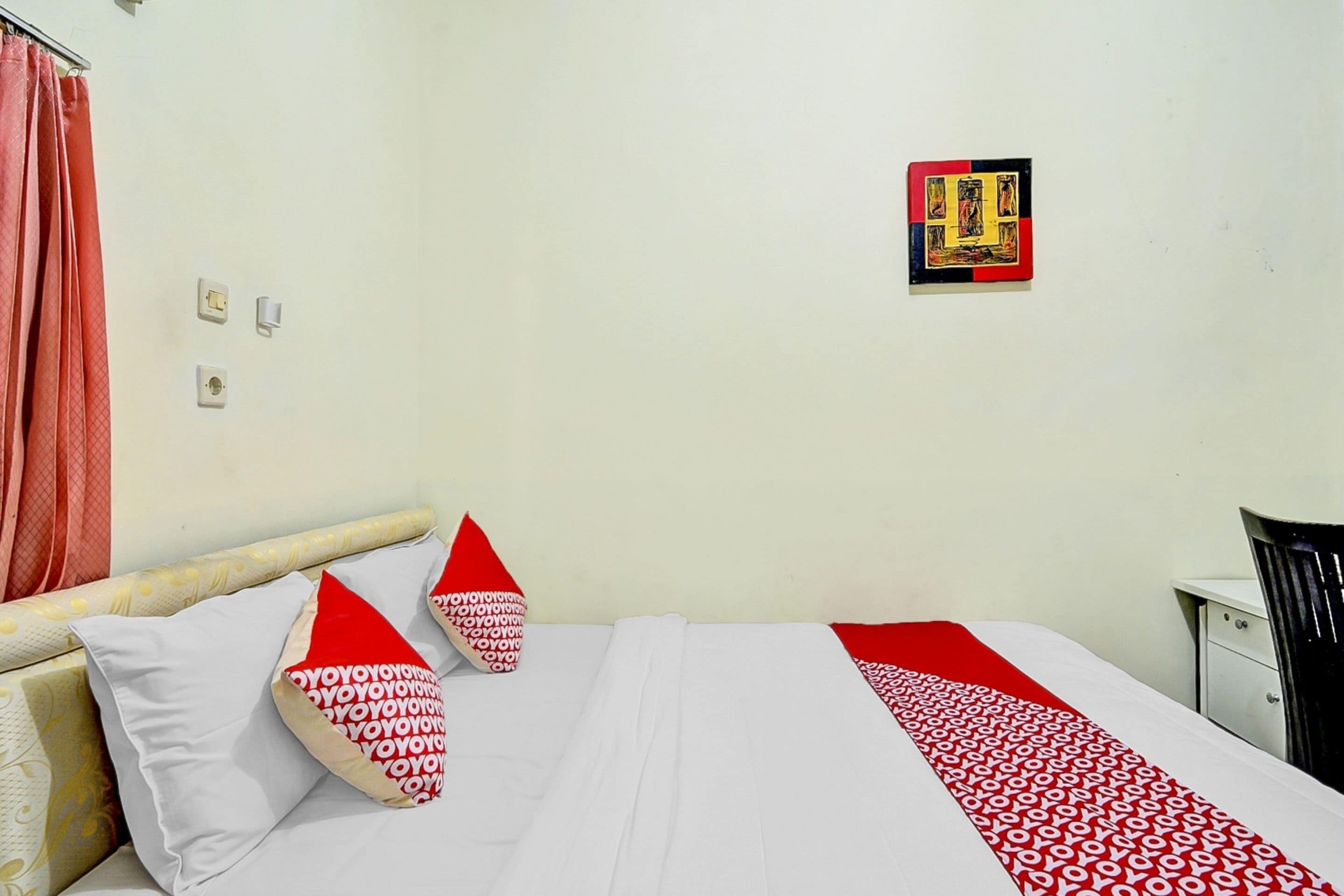 A hotel room with a bed, pillows, a nightstand, and a wall-mounted picture.