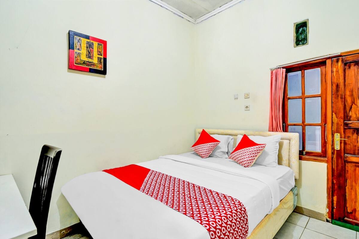 Een slaapkamer met een bed, een stoel, een deur en een aan de muur hangend schilderij.