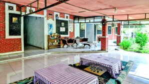 A spacious room with a high ceiling, a brick wall, and a large window. There are two tables with purple checkered tablecloths and a sofa. - OYO 90222 Lafa Park Syariah (Cikarang)