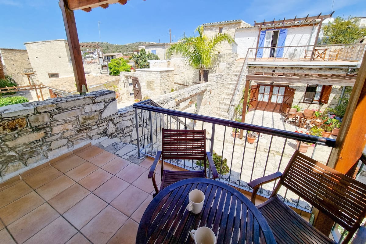 Ein Balkon mit Steinmauern, einer Holzpergola und Blick auf traditionelle Gebäude.