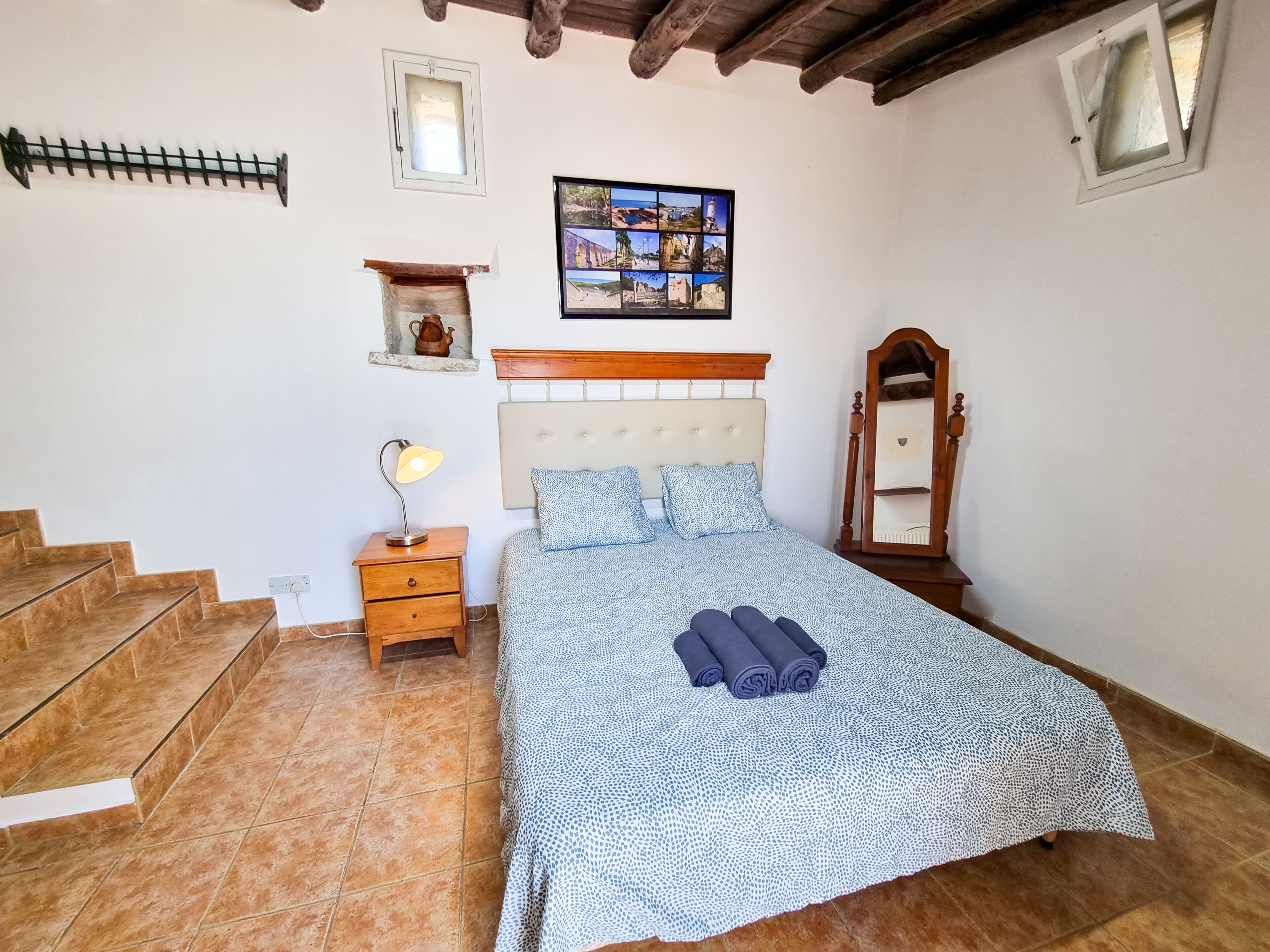 A bedroom with a bed, a nightstand, a lamp, a mirror, and a wall-mounted shelf.