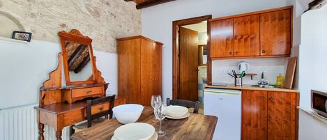 A rustic kitchen with wooden cabinets, a dining table set for two, and a refrigerator.