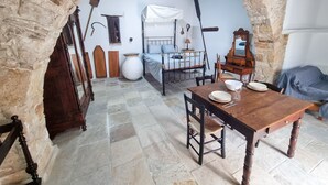 Une pièce rustique avec une arche en pierre, un lit avec un cadre en métal, une table en bois avec des assiettes et un sol en pierre.