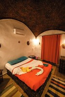 Una habitación acogedora con techo de ladrillo curvo, una cama con manta roja y una pequeña mesa con silla.