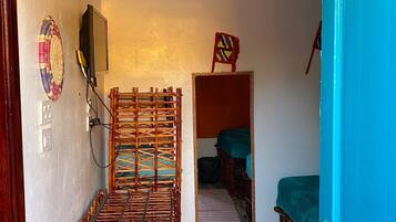 Quarto compacto com cama, espelho, TV fixada na parede e porta com moldura azul.