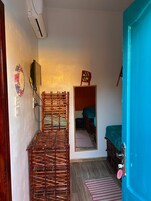 Quarto compacto com cama, espelho, TV fixada na parede e porta com moldura azul.