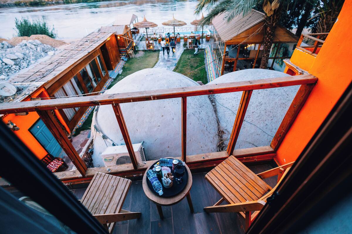 A balcony with wooden furniture, a table with drinks, and a view of a pool area.