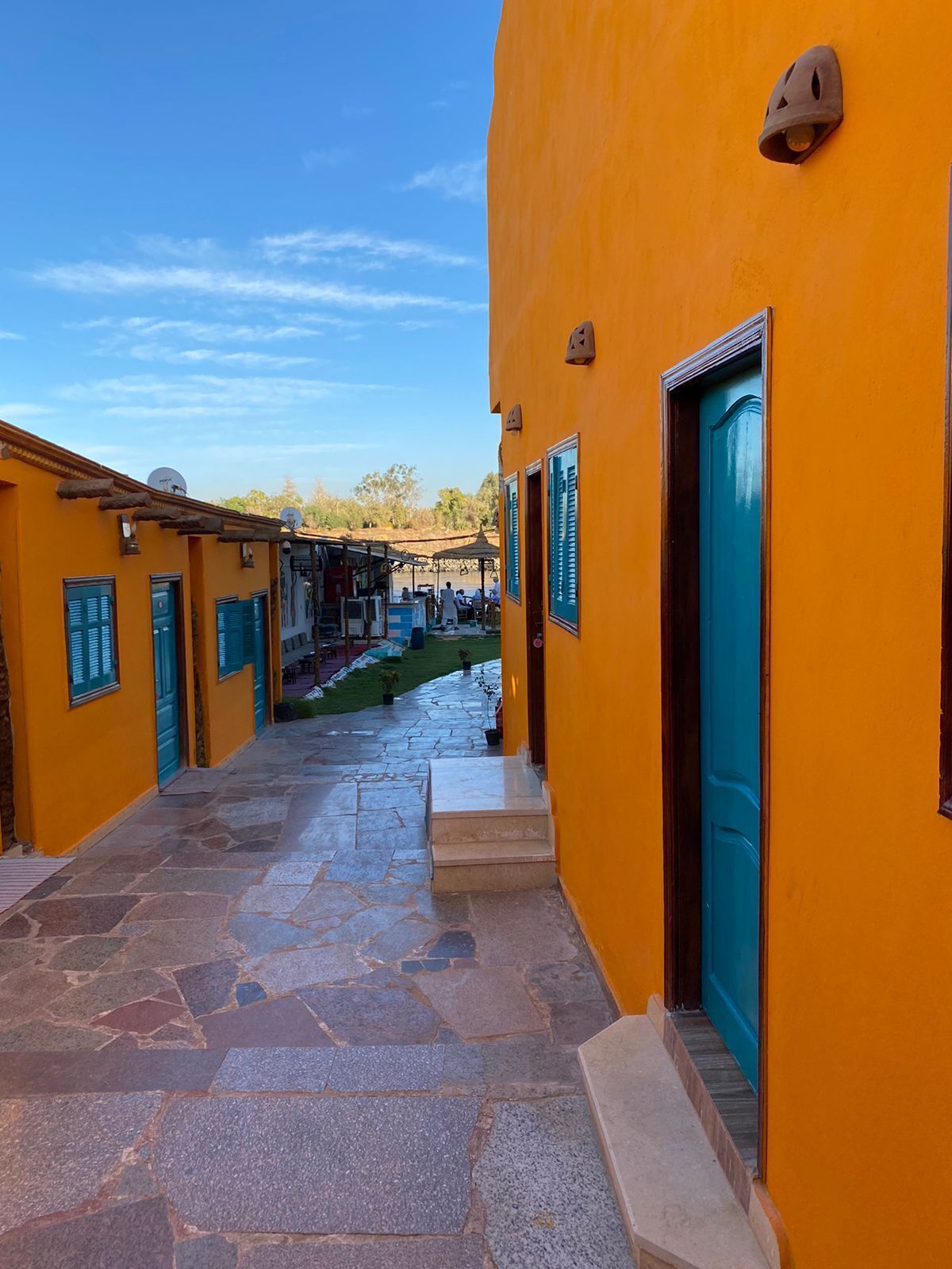 A narrow alleyway with stone pavement leading to a building with a bright orange facade and a blue door.