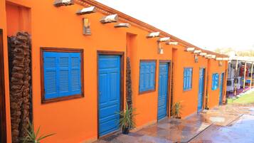 Une rangée de bâtiments orange avec des portes et des volets bleus, des escaliers en pierre et des plantes en pot.