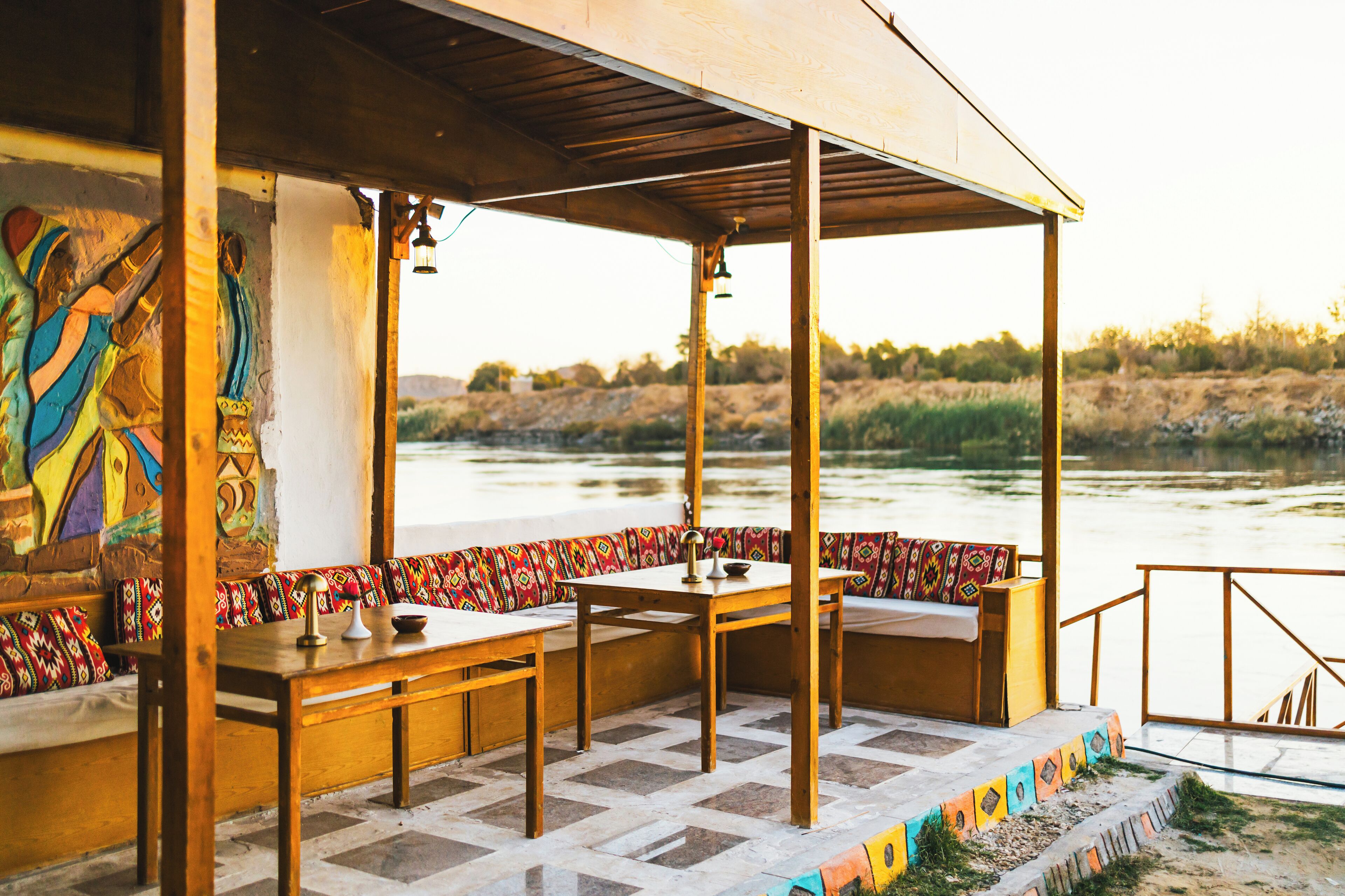 Un espacio de estar al aire libre cubierto, con mesas y bancos de madera, con vista a un río.