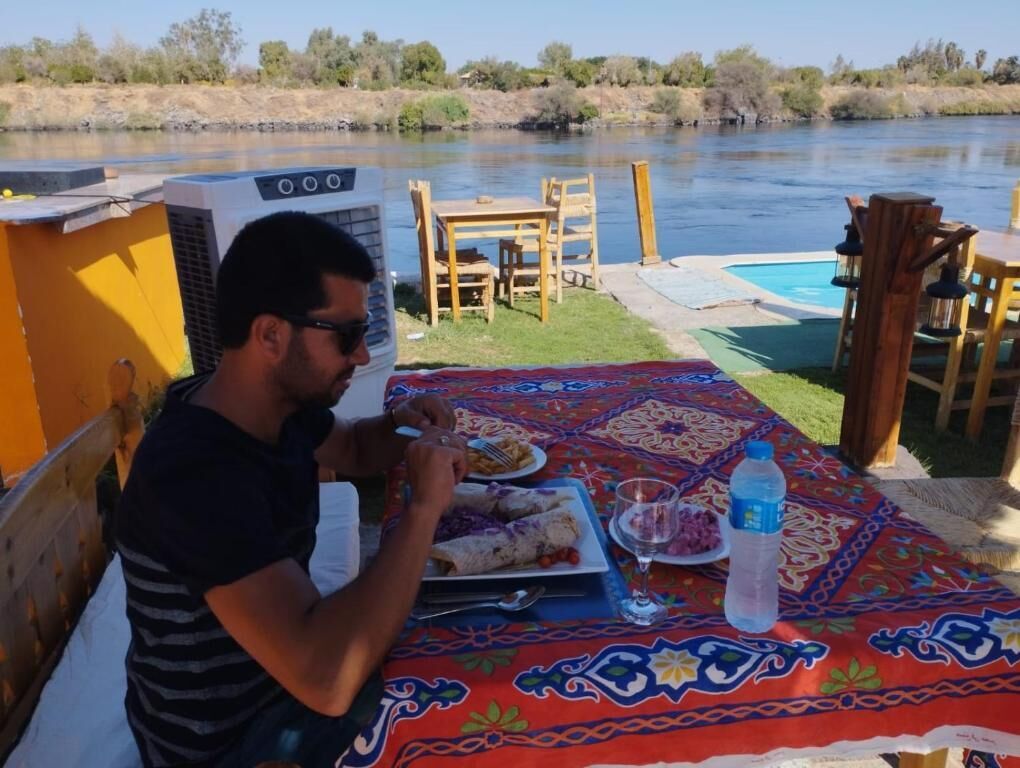 A dining area with a table set for two, a pool, and a river view.