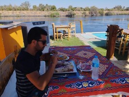 Comedor con mesa para dos, piscina y vista al río.