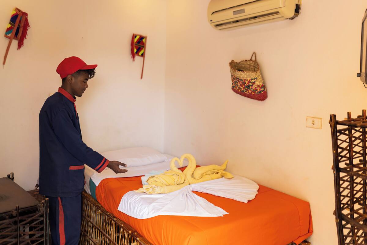 A hotel room with a bed, a suitcase, and a wall-mounted air conditioner.