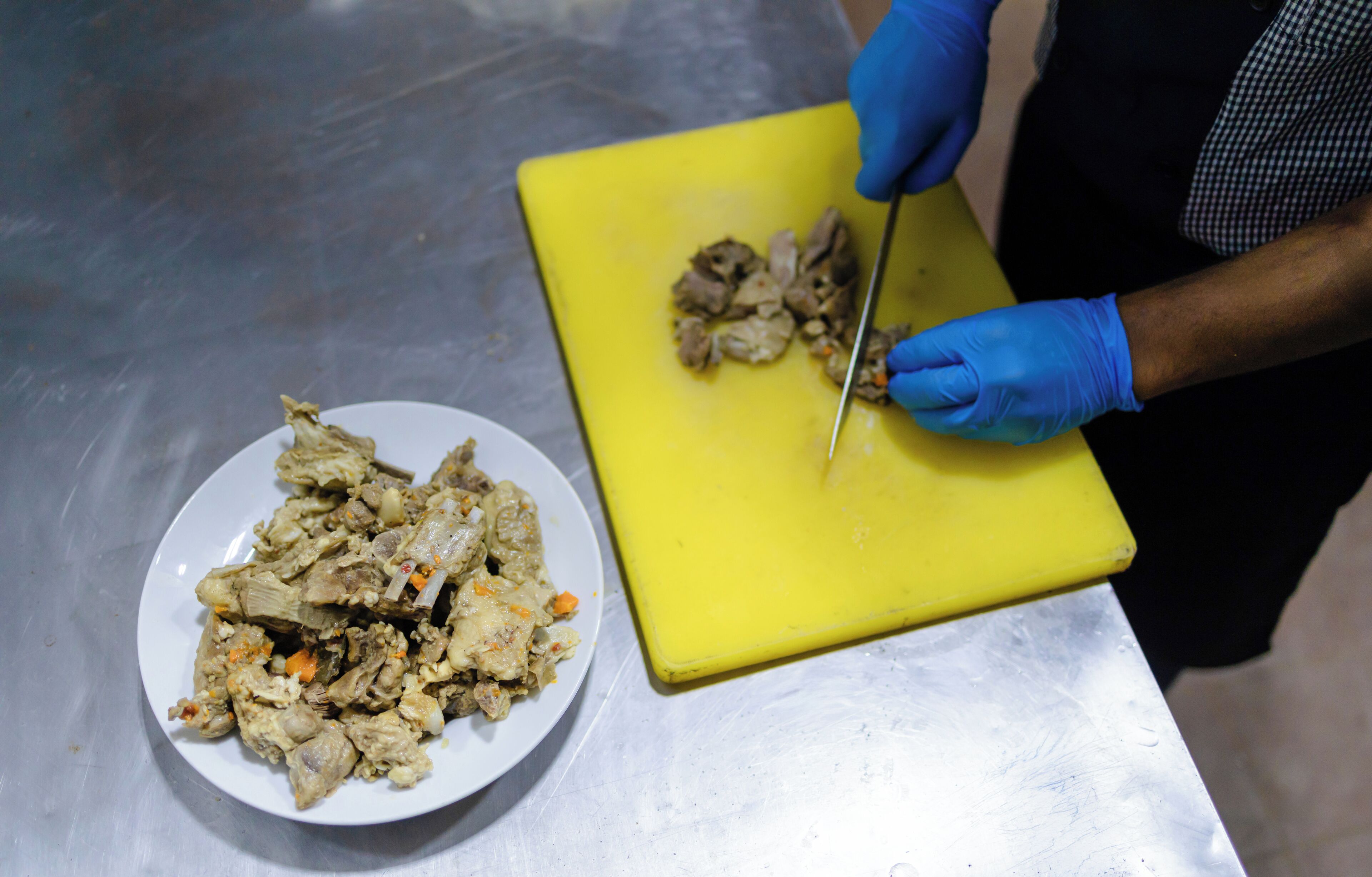A person wearing blue gloves cutting food on a yellow cutting board.