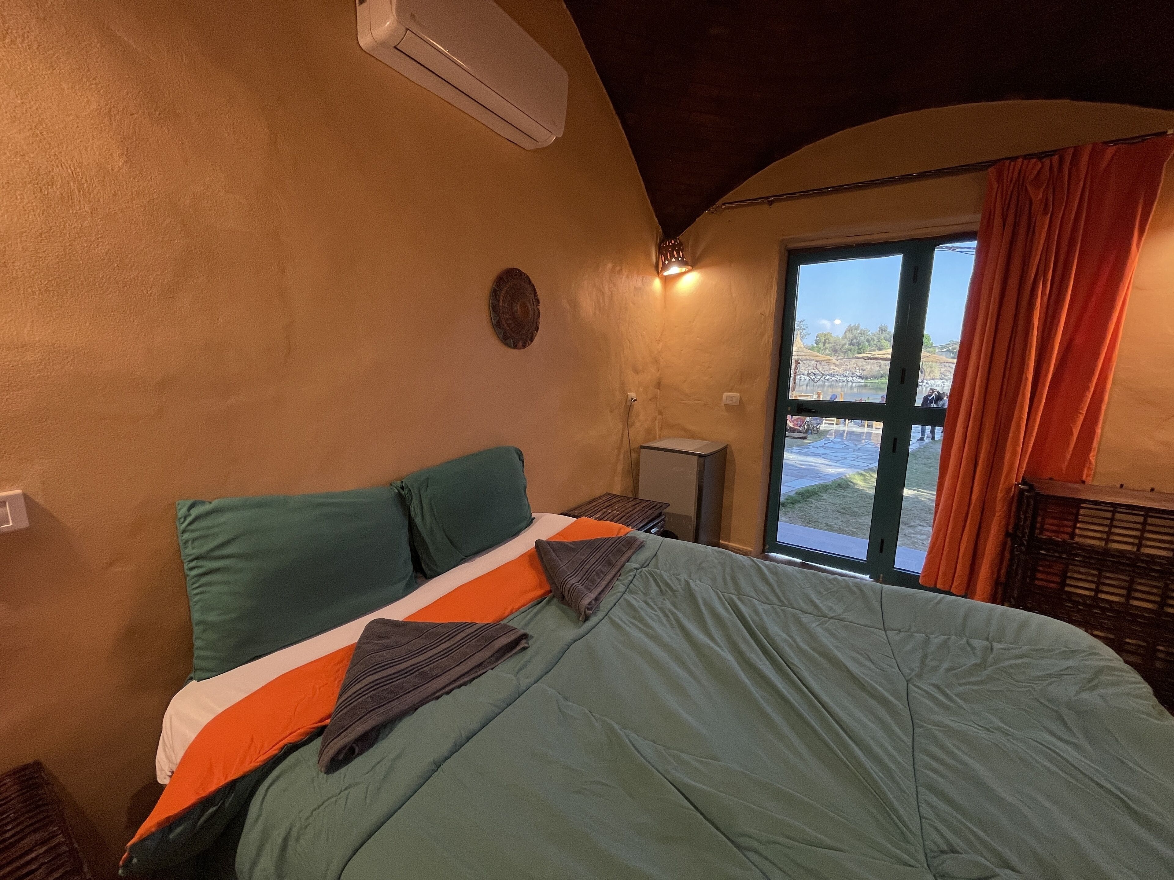 Une chambre à coucher avec un lit, un petit bureau, une fenêtre avec des rideaux et un climatiseur fixé au mur.