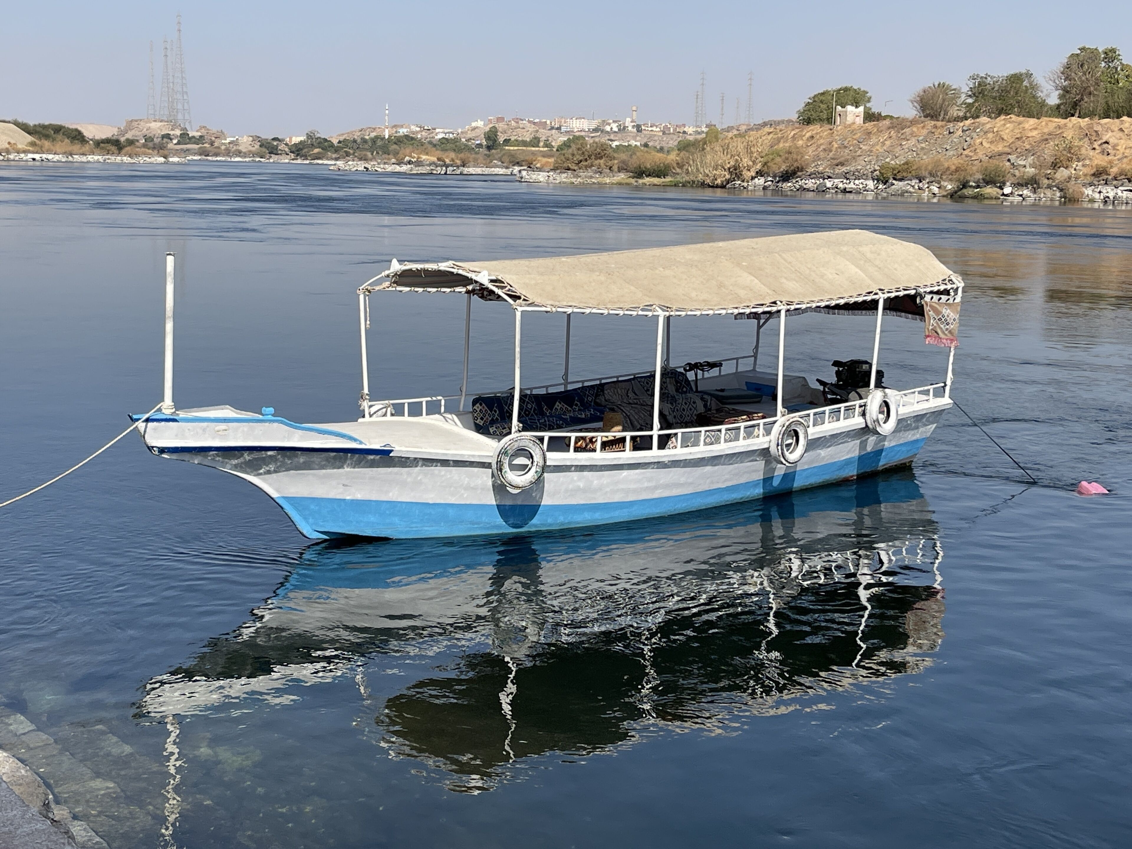 A boat with a covered deck, anchored in calm water.