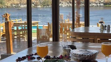 Un comedor con vistas a un lago, con una mesa dispuesta con comida y bebidas, y un cartel que indica servicio de transporte gratuito hacia el aeropuerto.