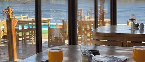 Un comedor con vistas a un lago, con una mesa dispuesta con comida y bebidas, y un cartel que indica servicio de transporte gratuito hacia el aeropuerto.
