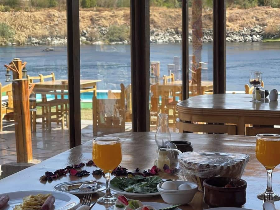 Una mesa de comedor lista con platos de comida, vasos y vistas a una masa de agua a través de amplios ventanales.