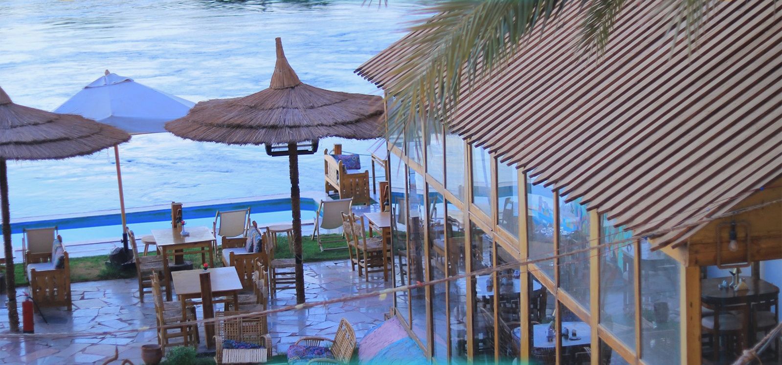 A beachfront restaurant with outdoor seating, umbrellas, and a view of the sea.