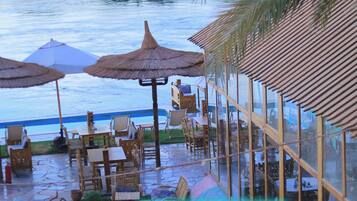 A beachfront restaurant with outdoor seating, umbrellas, and a view of the sea.