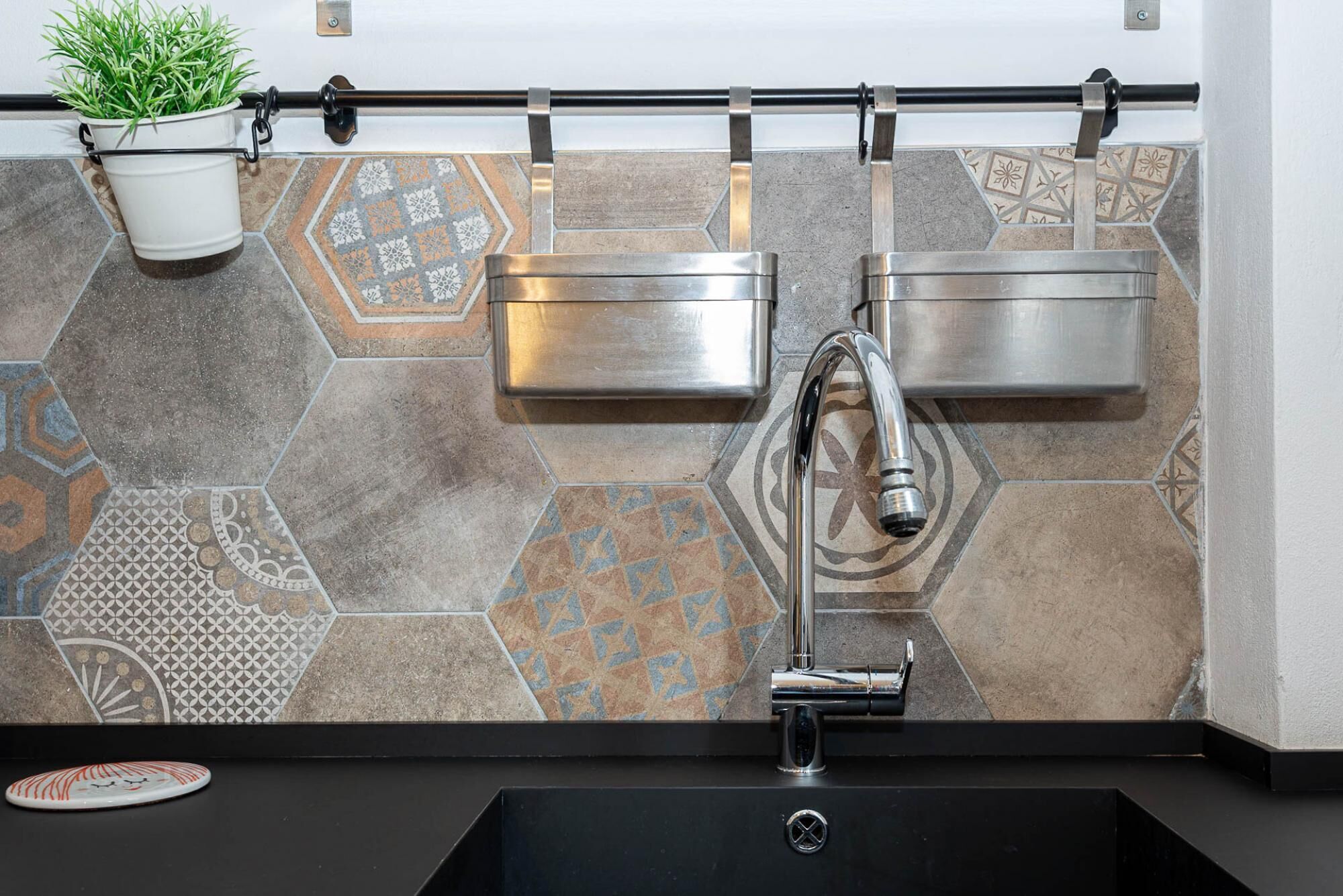 A bathroom with a black sink, two stainless steel towel dispensers, and a potted plant.