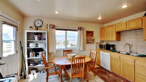A compact kitchen with wooden cabinets, a dining table with chairs, a clock, and a view of the mountains through the window. - Cozy country-style home, relaxing views off the deck, and dog friendly! (Silverthorne)
