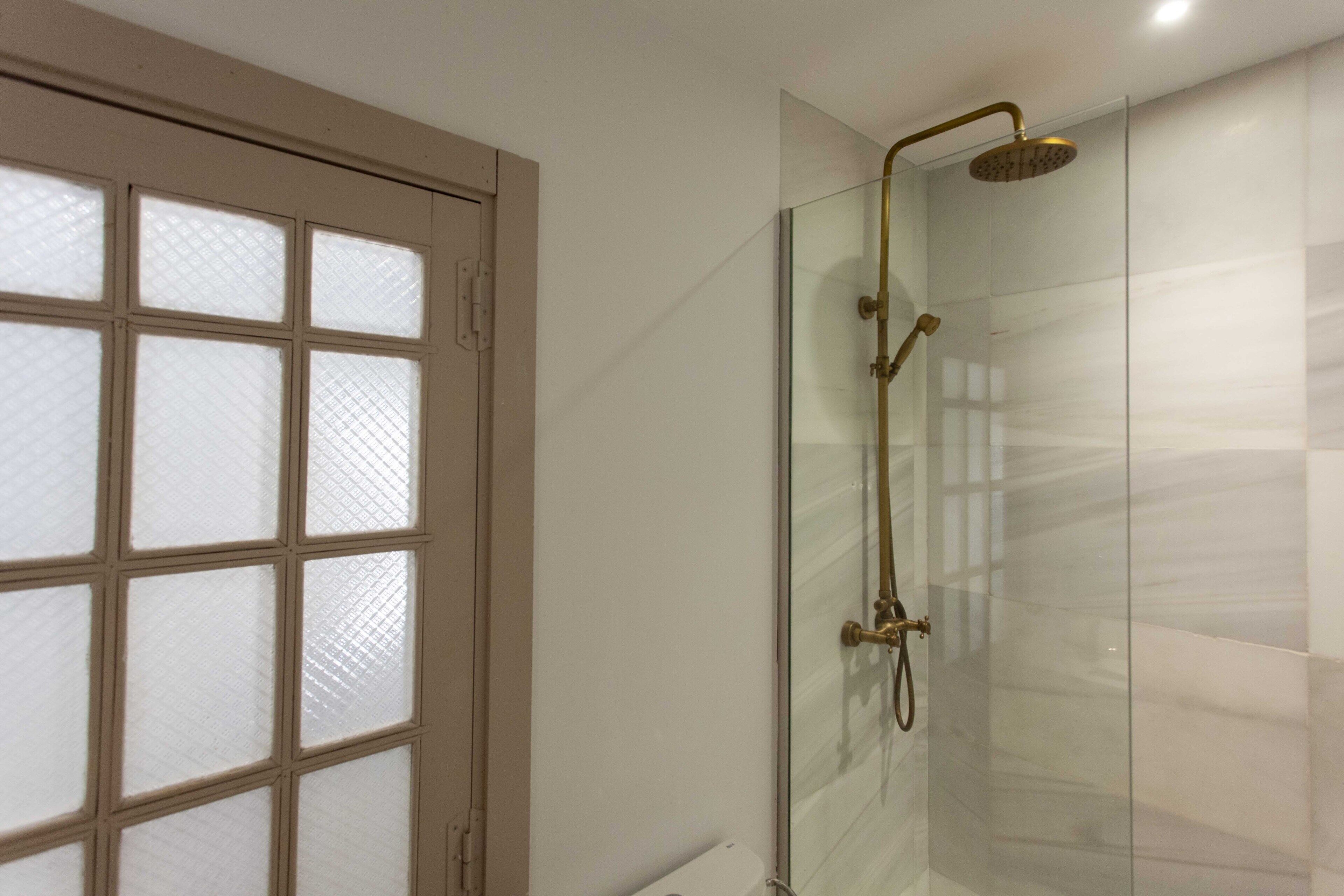 Une douche fermée par des parois en verre, dotée d’un pommeau de douche doré et d’un pommeau de douche à main.