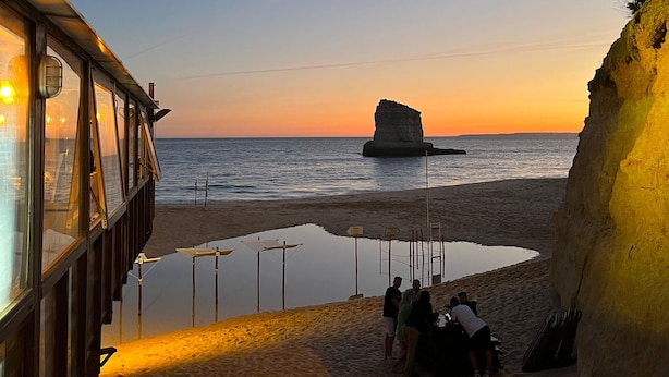 Una playa con una formación rocosa, una piscina y un edificio con ventanas amplias.