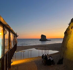 A beach with a rock formation, a pool, and a building with large windows. - Villa Gaivota CasAmar (Parque de Campismo)