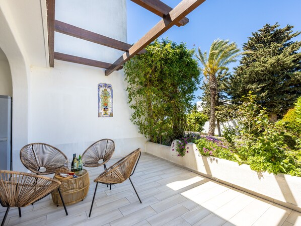 A terrace with wicker chairs, a small round table, and a decorative tile. - Villa Gaivota CasAmar (Parque de Campismo)