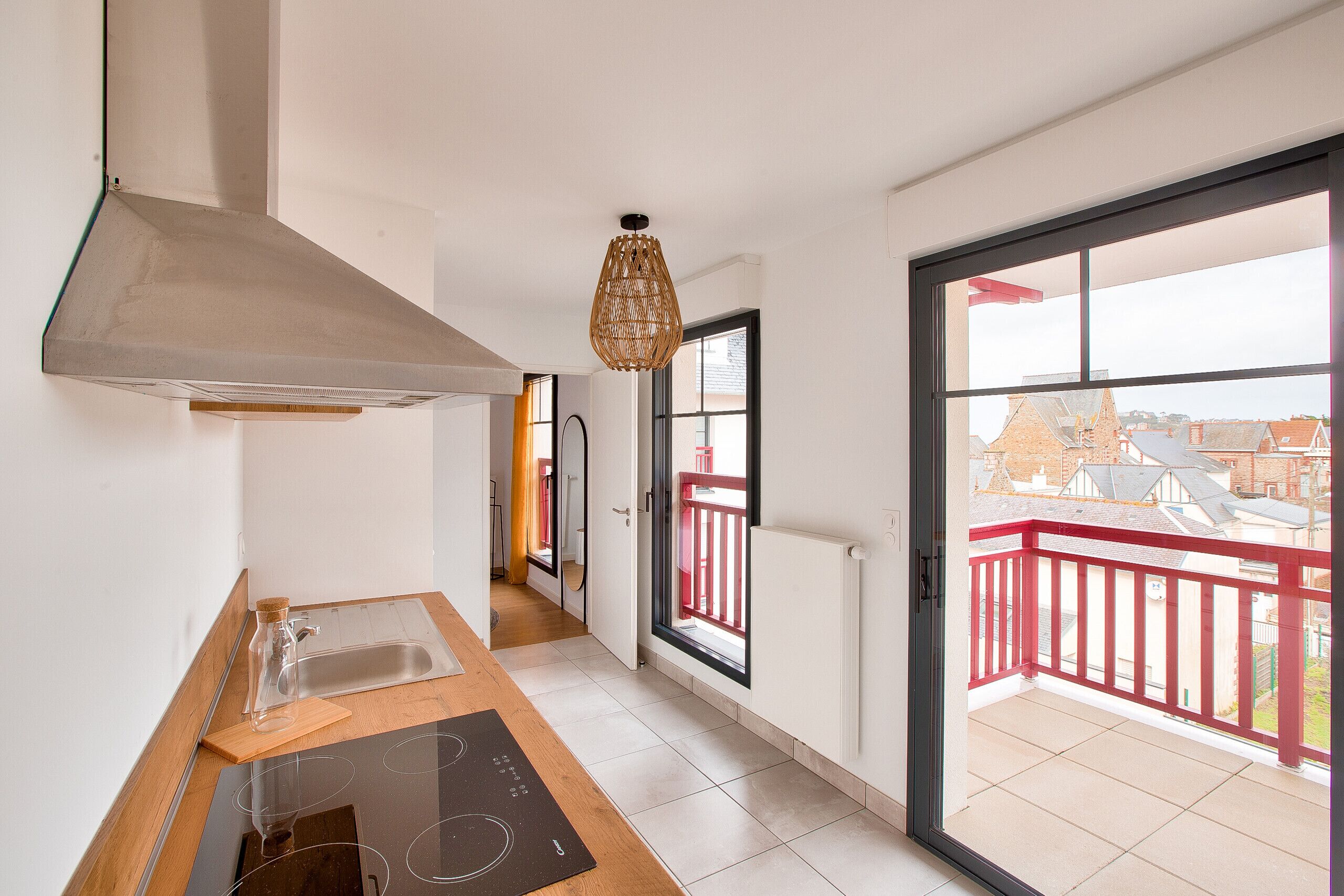 Een moderne keuken met een groot raam, een rood balkon en uitzicht op de omgeving.