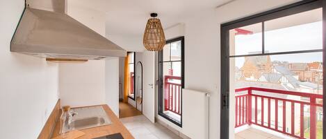 Een moderne keuken met een groot raam, een rood balkon en uitzicht op de omgeving.