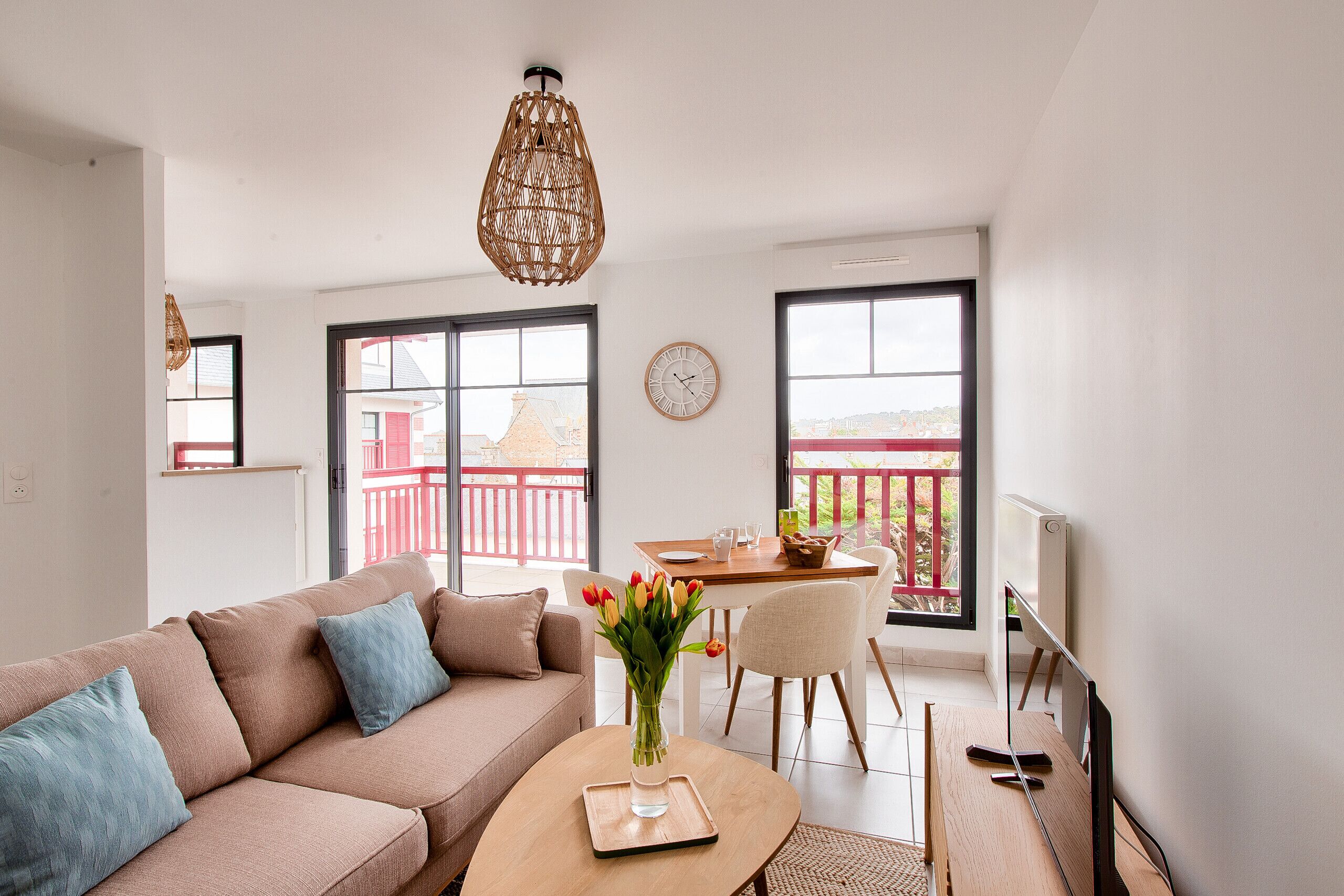 Ein modernes Wohnzimmer mit einer Couch, einem Couchtisch, einem Esstisch mit Stühlen, einer Hängeleuchte und Blick ins Freie durch große Fenster.