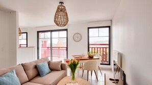 Un salon moderne comprenant un canapé, une table basse, une table à manger avec des chaises, un luminaire suspendu et une vue sur l’extérieur grâce à de grandes fenêtres.