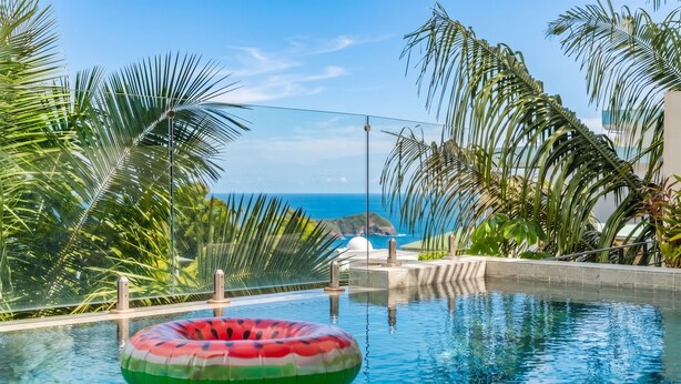 Una piscina con vista al océano, rodeada de palmeras.