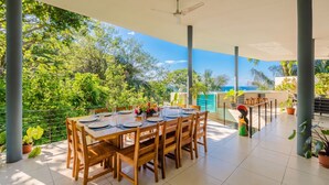 Un área de comedor al aire libre cubierta con una mesa dispuesta para cuatro personas, rodeada de macetas con plantas y vistas al mar.