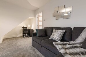 Cozy attic space with a desk for work or study, featuring a sofa and large window.