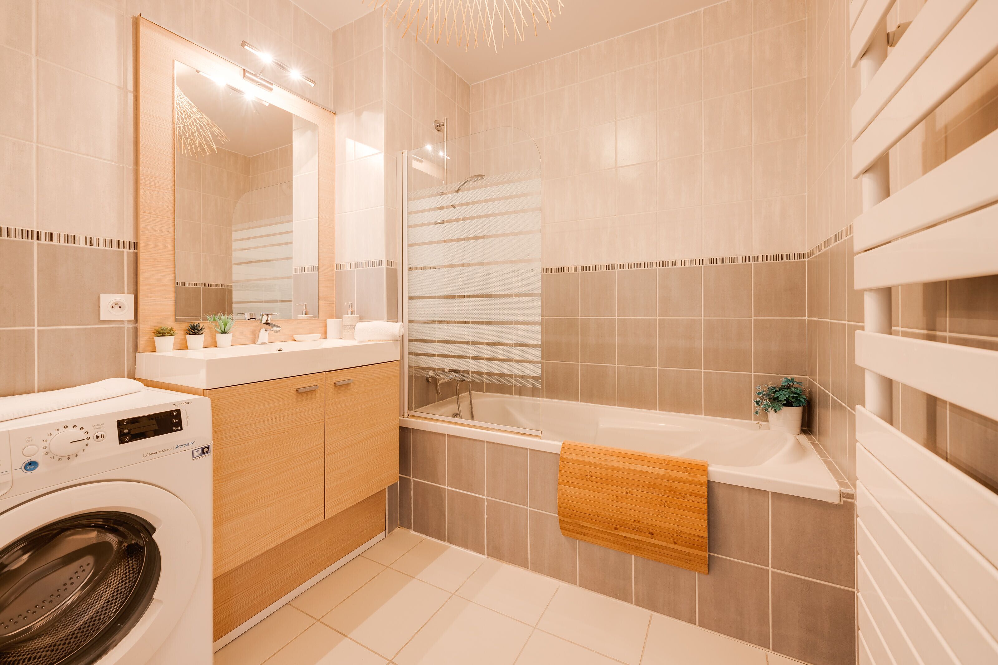 A modern bathroom with a washing machine, a bathtub, and a large mirror.