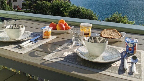 Un coin petit-déjeuner aménagé avec une vue pittoresque sur un lac, comprenant des montagnes et une petite maison en arrière-plan.