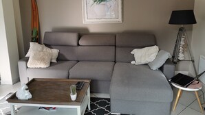 Un salon moderne avec un canapé d’angle gris, une table basse, une lampe et un ordinateur portable posé sur une table d’appoint.