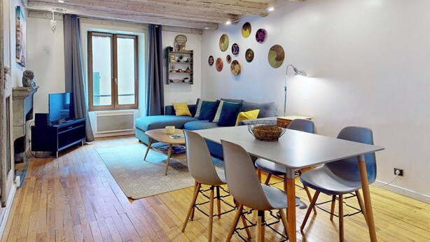 A modern living room with a wooden ceiling, a sofa with cushions, a dining table with chairs, and a fireplace. - Le Cocon Rousseau - Pretty T2 in Old Town (Annecy)
