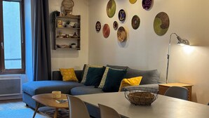 A modern living room with a gray sofa, a dining table with chairs, and a floor lamp. - Le Cocon Rousseau - Pretty T2 in Old Town (Annecy)