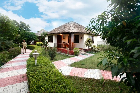 A bungalow with a thatched roof, surrounded by a well-maintained garden with a brick pathway. - Vanasthali Jungle Resort Jim Corbett (Ramnagar)