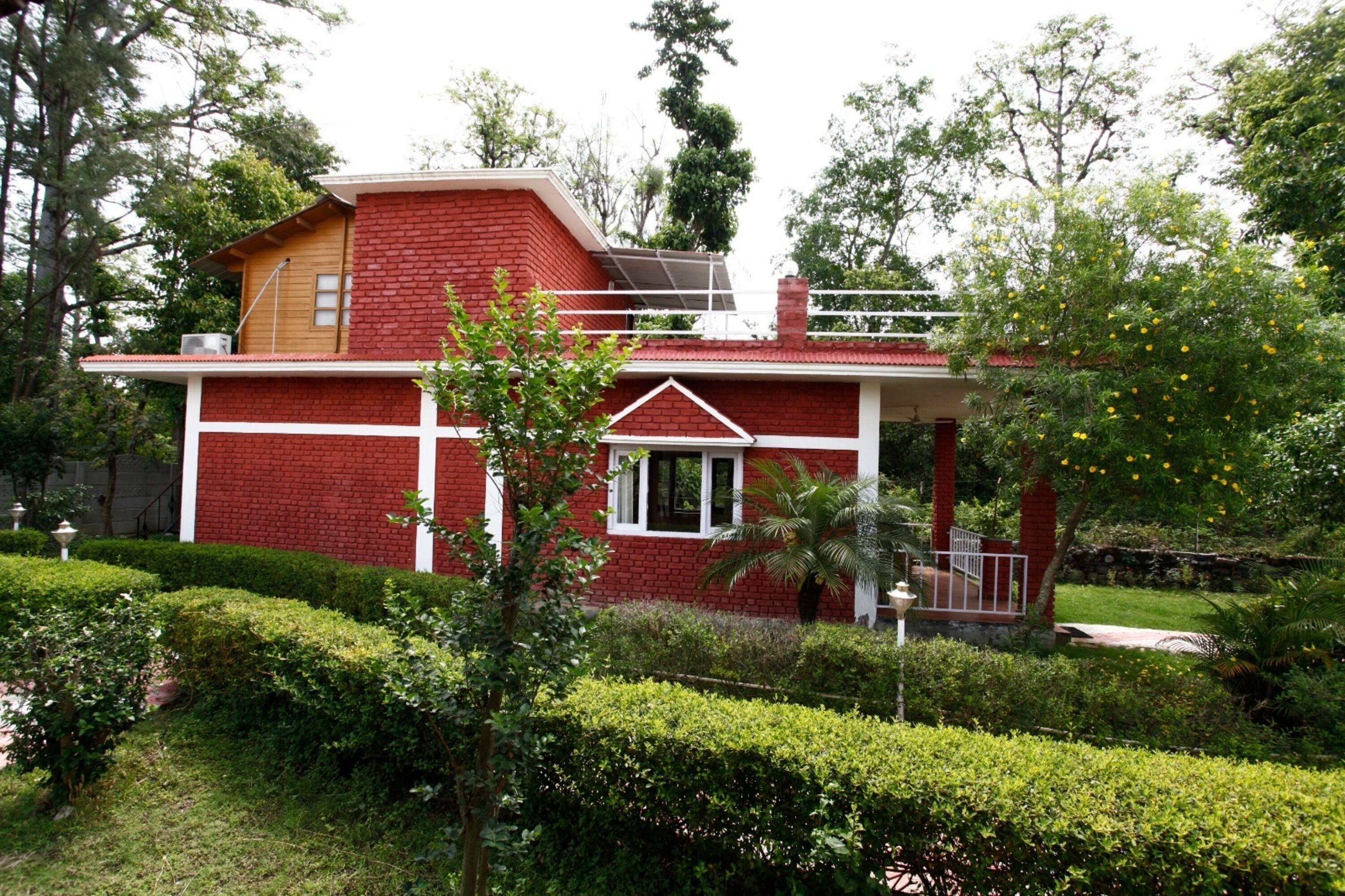 A red brick house with a balcony, surrounded by well-maintained hedges and trees.