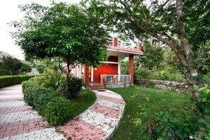 A red brick house with a white porch, surrounded by lush greenery and a brick pathway. - Vanasthali Jungle Resort Jim Corbett (Ramnagar)