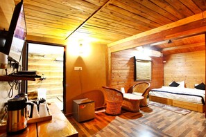 A cozy room with a bed, a TV, a coffee maker, and wicker chairs. - Vanasthali Jungle Resort Jim Corbett (Ramnagar)