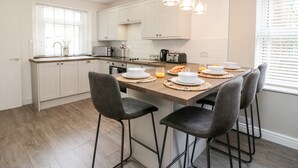 Cozinha moderna com armários brancos, bancada de madeira e área de refeições com quatro cadeiras.